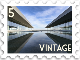 May 2022 Vintage SWG challenge stamp - A modern concrete and glass building consisting of two wings on either side of a reflecting pool. There are strong diagonal lines formed by the roof of each wing and their reflections.