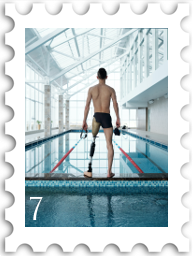 July 2022 Zingers SWG challenge stamp - color photo of a swimmer in a natotorium. The swimmer stands on the bulkhead between the diving pool and racing pool, facing away from the camera. The swimmer is a full leg amputee. 