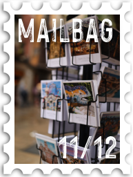 November/December 2022 Manwë's Mailbag SWG challenge stamp - color photo of an outdoor postcard rack, with the text "Mailbag" and number 11/12