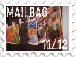 November/December 2022 Manwë's Mailbag SWG challenge stamp - color photo of a number of colorful postcards suspending on a string by clothespins, with the text "Mailbag" and number 11/12