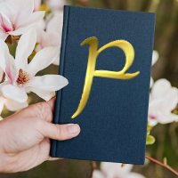 parma tengwa on cover of a blue clothbound book held against a background of flowers