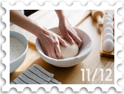 November/December 2025 Great Beleriand Bake-Off SWG challenge stamp - a photo of a pair of hands setting a doug ball into a proving basket. A bowl of flour and rack of eggs are visible to either side.