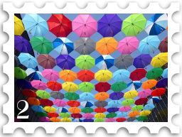 February 2026 Title Track SWG challenge  stamp - a photo of a display of colorful umbrellas against a blue sky. There are dozens of umbrellas in many bright colors.