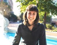 female with shoulder length hair and black shirt sitting in front of fountain and trees
