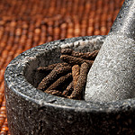 Photo of a granite mortar and pestle with long peppercorns in it on a woven red background, by djwtwo on flickr.