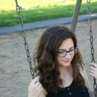 A picture of me, brunette, wavy-haired girl in a black dress, seated on a swing. 