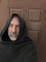 The presumed author in woolen  green cloak look at viewer , a brown wooden  door is in  the  background