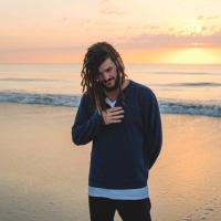 A man stands on the beach with the sun setting behind him. 