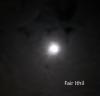 White hazy moon among light clouds in black night sky. Caption in white in bottom right corner.